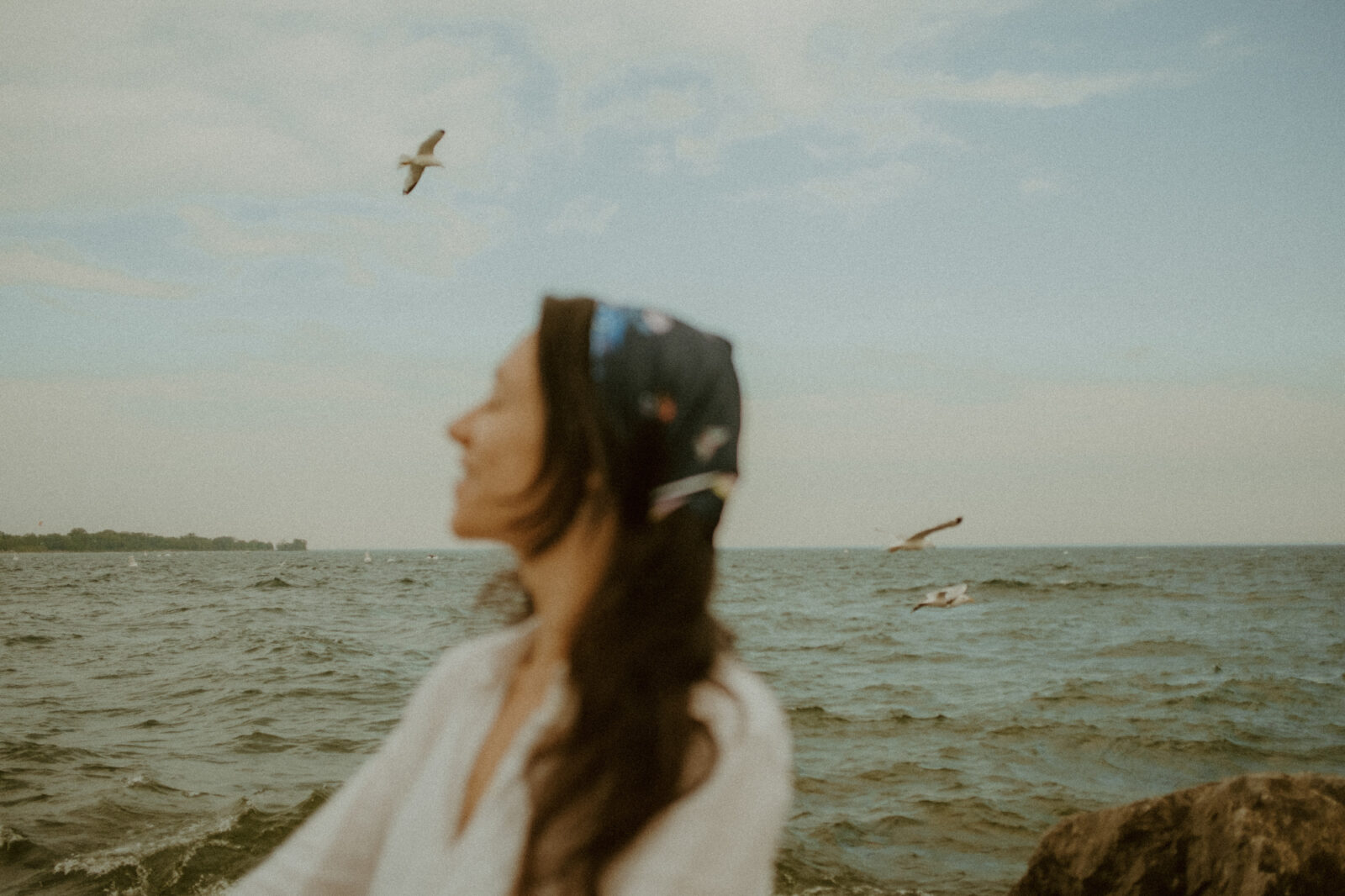 Woman closing her eyes as she sits near water with birds in background